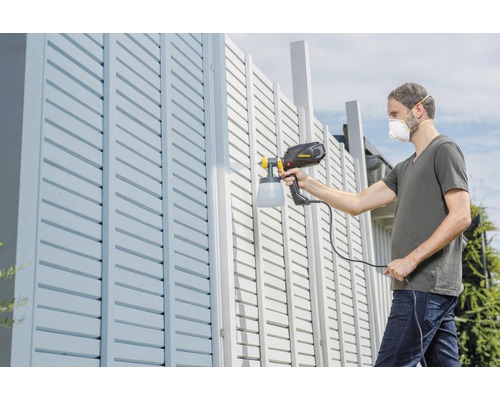 Muž strieka plot pomocou striekacej pištole.