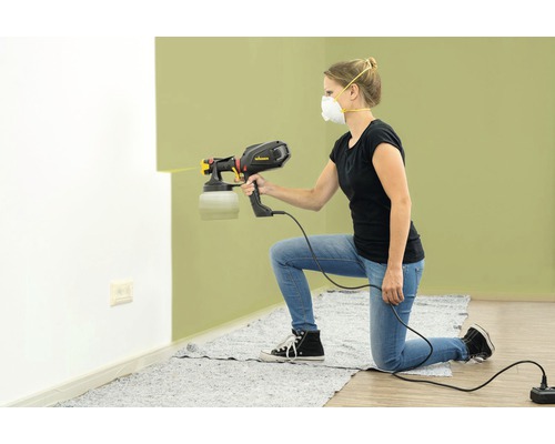 Žena používa striekaciu pištoľ na maľovanie steny.