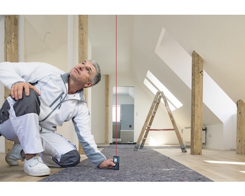 Remeselník používa laserový diaľkomer v podkroví na vykonávanie presných meraní.