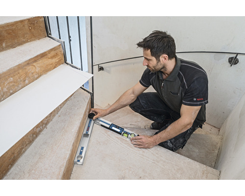 Remeselník meria schodisko uhlomerom. Logo Bosch