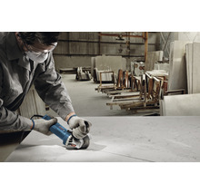 Robotník reže kamennú dosku uhlovou brúskou v dielni.