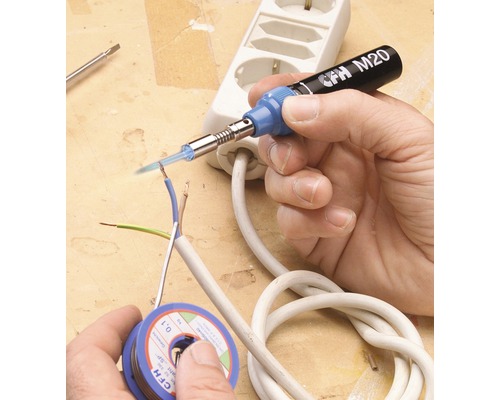 Ruka spájkuje elektrické vedenie spájkovačkou. Na stole leží cievka spájky a zásuvková lišta.