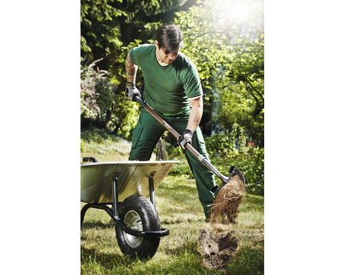 Muž kope rýľom v záhrade vedľa fúrika.