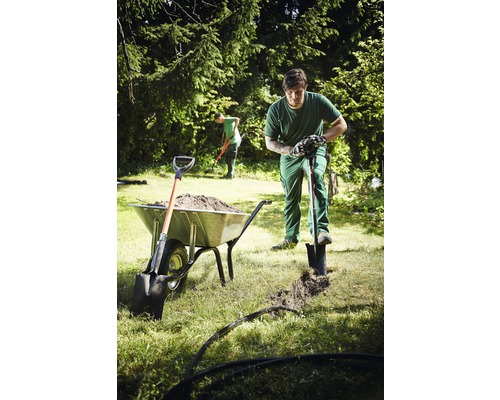 Záhradník kope priekopu rýľom vedľa fúrika plného hliny.