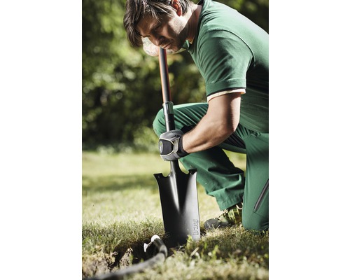 Muž kľačí v záhrade a kope rýľom dieru.