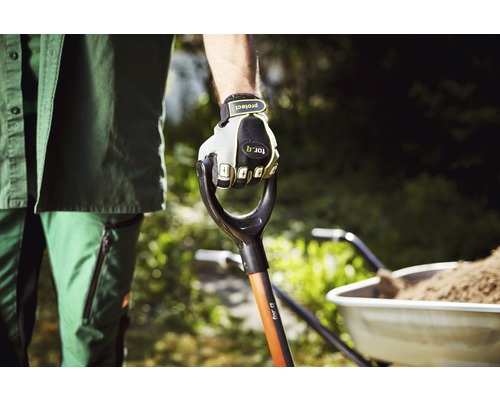 Záhradník drží rýľ v rukaviciach, fúrik v pozadí