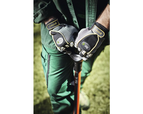 Osoba v pracovnom odeve drží rýľ v záhradných rukaviciach.