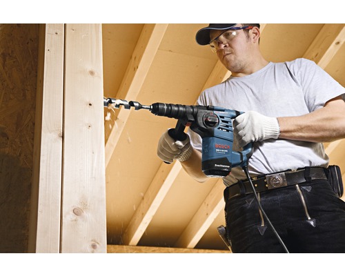 Remeselník vŕta dieru do drevenej dosky vŕtačkou Bosch.