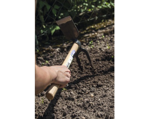 Ruka drží multifunkčnú motyku v záhradnej pôde