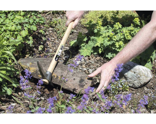 Osoba pracuje v záhrade s krompáčom s drevenou rukoväťou.