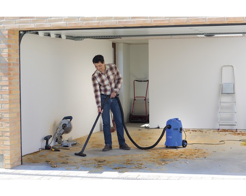 Muž vysáva triesky mokro-suchým vysávačom v garáži.