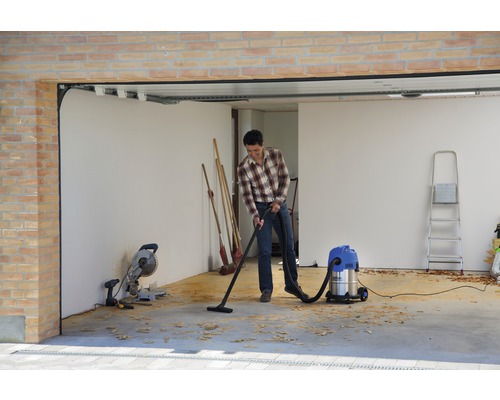 Muž vysáva garáž viacúčelovým vysávačom