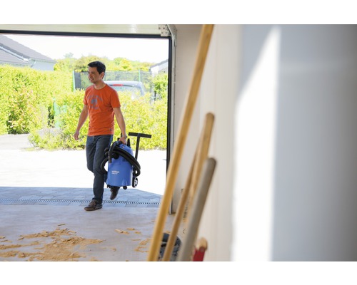 Muž vynáša mokrý a suchý vysávač z garáže.