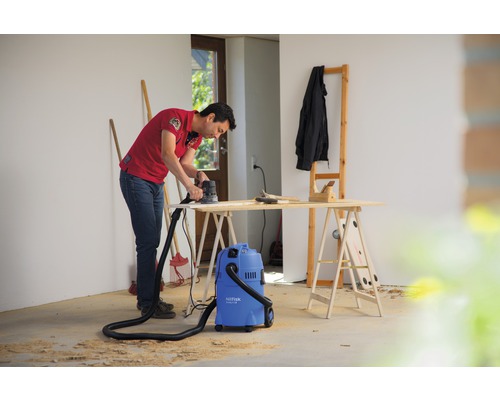 Muž brúsi drevo brúskou vedľa vysávača v dielni