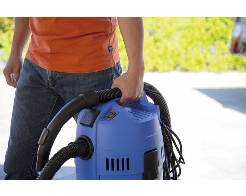 Osoba drží modrý viacúčelový vysávač s čiernou hadicou.