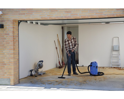 Muž vysáva piliny v garáži priemyselným vysávačom