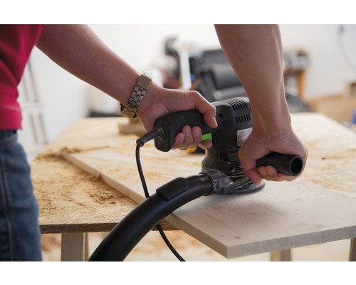 Osoba brúsi drevenú dosku excentrickou brúskou.