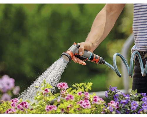 Osoba zavlažuje kvety pomocou záhradnej striekacej pištole Gardena.