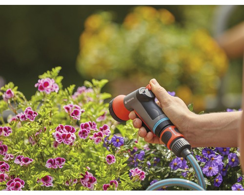 Záhradná scéna s osobou zalievajúcou kvety záhradnou striekacou pištoľou Gardena.