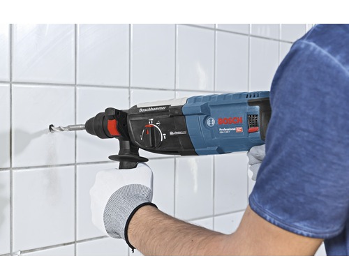 Osoba vŕta otvor do obkladanej steny pomocou vŕtacieho kladiva