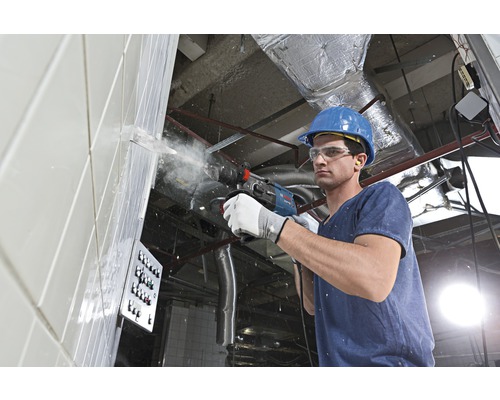 Stavebný robotník vŕta s vŕtacím kladivom do steny.