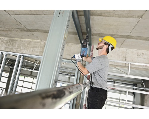 Remeselník vŕta vŕtačkou do kovového profilu na stavenisku.