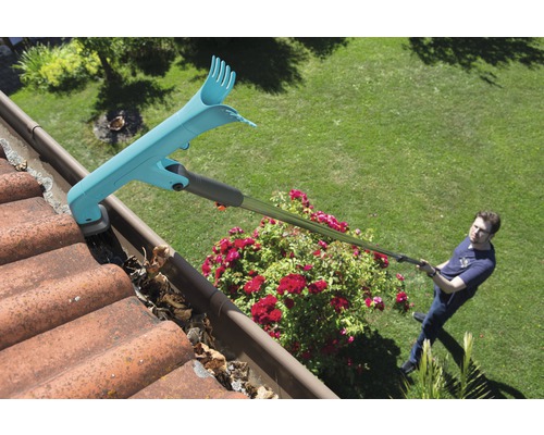 Muž čistí odkvapový žľab pomocou čističa odkvapov, pričom odstraňuje lístie.