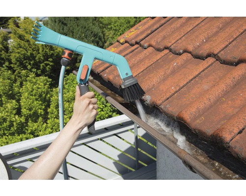 Osoba čistí odkvap pomocou kefy na odkvapy a záhradnej hadice.