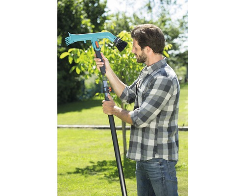 Muž so záhradnou kefou s teleskopickou rukoväťou v záhrade.