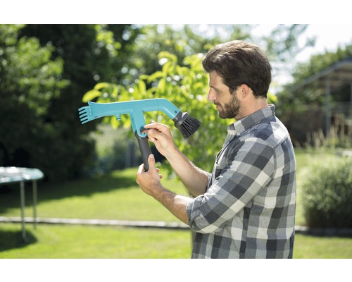 Muž obsluhuje kefu na odkvapy v záhrade.