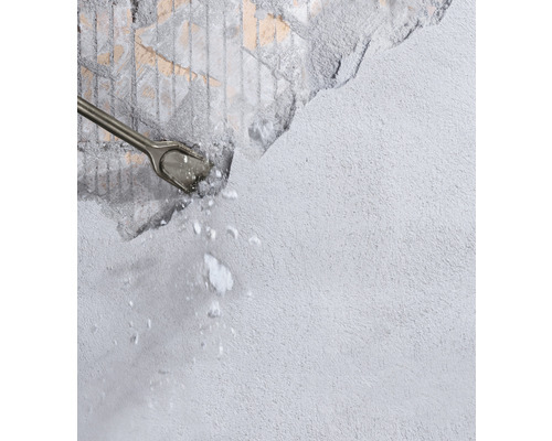 Sekáč opracováva sivú stenu a vznikajú úlomky kameňa.