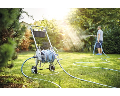 Záhradná scéna s hadicovým vozíkom a osobou zavlažujúcou trávnik