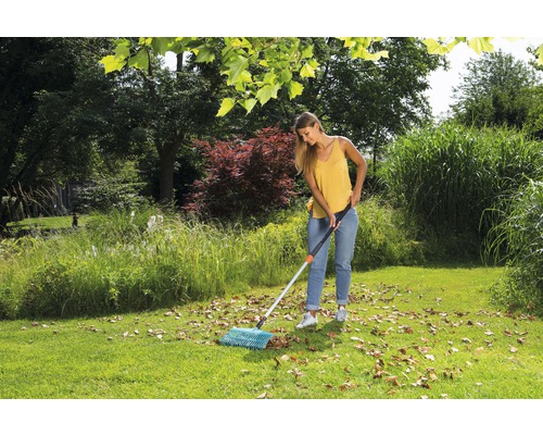 Žena zametá lístie vejárovými hrabľami v záhrade.