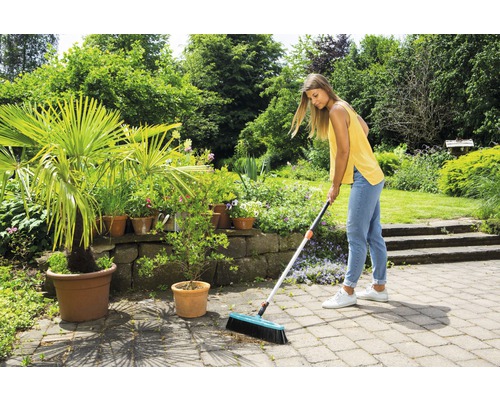 Žena zametá kamennú terasu s pouličnou metlou v záhrade