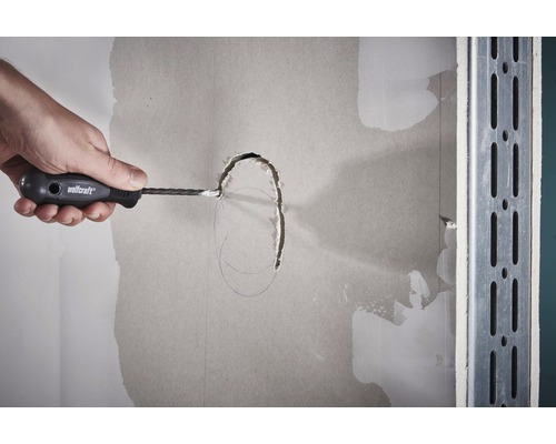 Ruka vyrezáva sadrokartónovým rezačom otvor do sadrokartónovej steny.