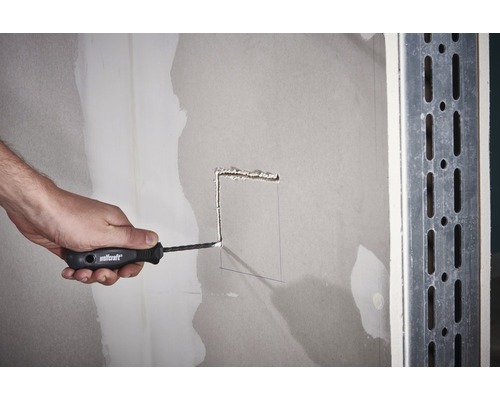 Osoba vyrezáva dieru do sadrokartónovej steny pomocou rezacieho noža.