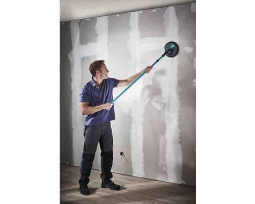 Muž brúsi stenu brúskou s dlhým krkom