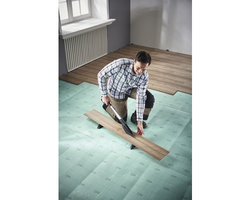 Muž reže laminát pomocou rezačky laminátu na izolačnej podložke v miestnosti