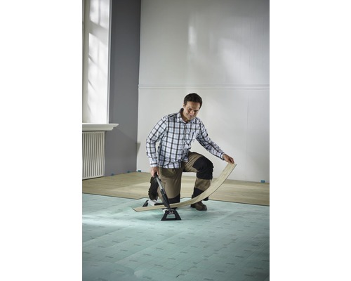 Muž pokladá laminát pomocou rezačky laminátu v miestnosti.