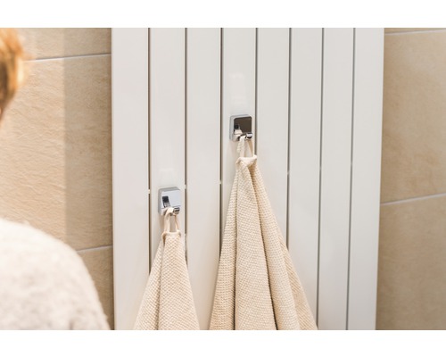 Biely radiátor s dvoma uterákmi a chrómovými háčikmi v kúpeľni.