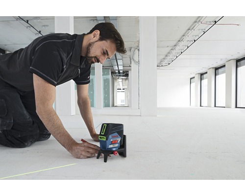 Muž používa krížový čiarový laser Bosch na stavenisku na nakreslenie čiary na podlahu.