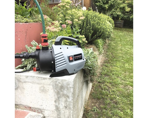 Záhradné čerpadlo s hadicou na betónovom podstavci v záhrade