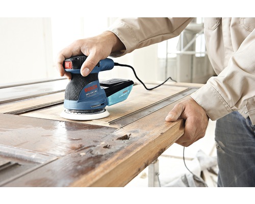 Muž používa excentrickú brúsku Bosch na brúsenie drevených dverí.