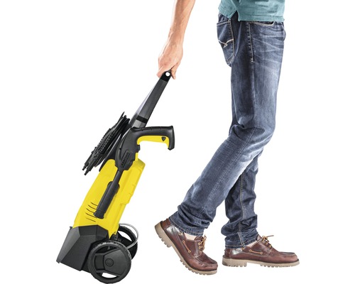 Osoba tlačí žltý vysokotlakový čistič s kolieskami.