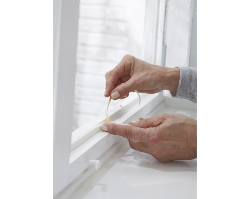 Osoba aplikuje tesniacu pásku na okno.