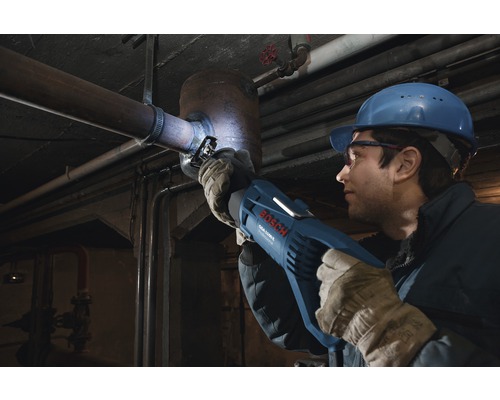 Muž s ochrannou helmou a okuliarmi reže rúru pomocou šabľovej píly Bosch.