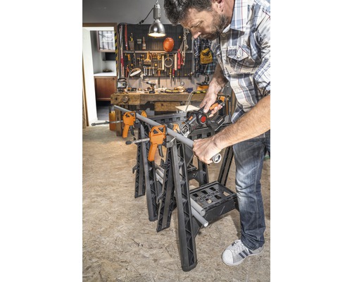 Muž reže rúru na pracovnom stole so svorkami a chvostovou pílou v dielni.