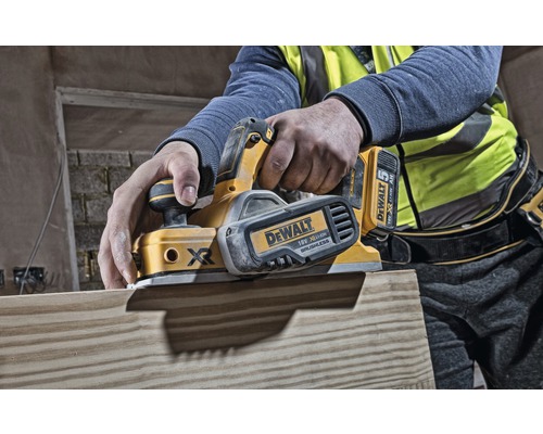 Osoba hobľuje drevenú dosku elektrickým hoblíkom. Hoblík je od spoločnosti DeWalt.