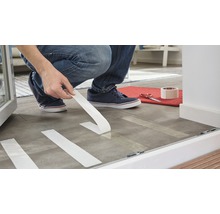 Osoba pripevňuje lepiacu pásku na podlahu na prípravu na renováciu.