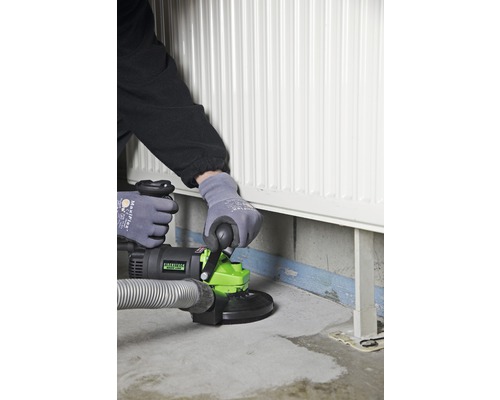 Osoba používa brúsku na betón v blízkosti radiátora.